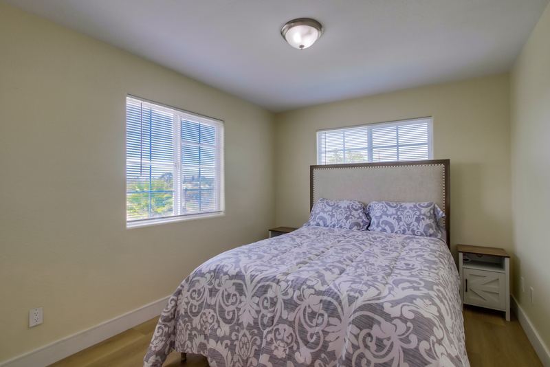 A bedroom with a grey patterned bedspread, an upholstered headboard and two windows