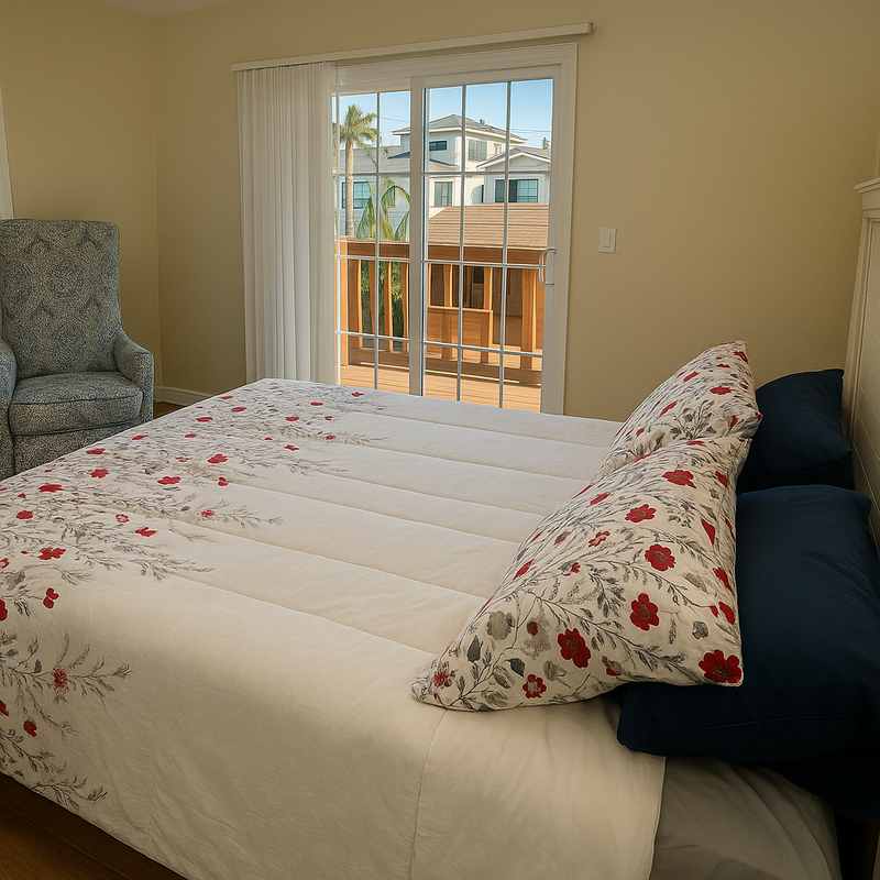 A bedroom with a large bed in floral and white bedding, an armchair in the corner and a door onto the balcony