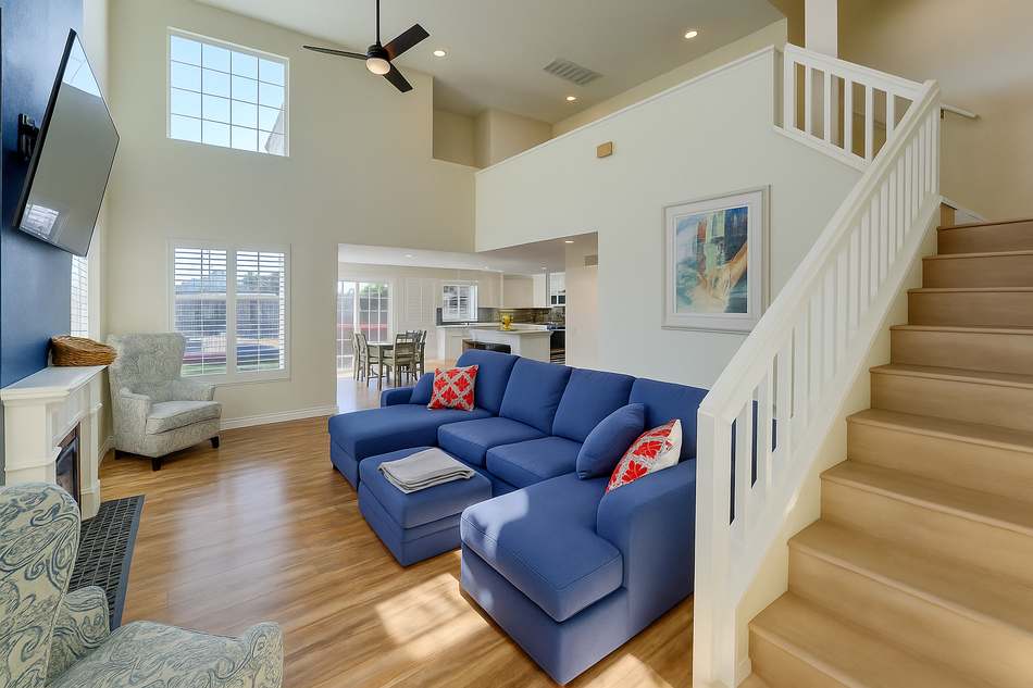The living room: a double-height ceiling, a blue sectional facing a wall-mounted television, and a staircase rising to the landing